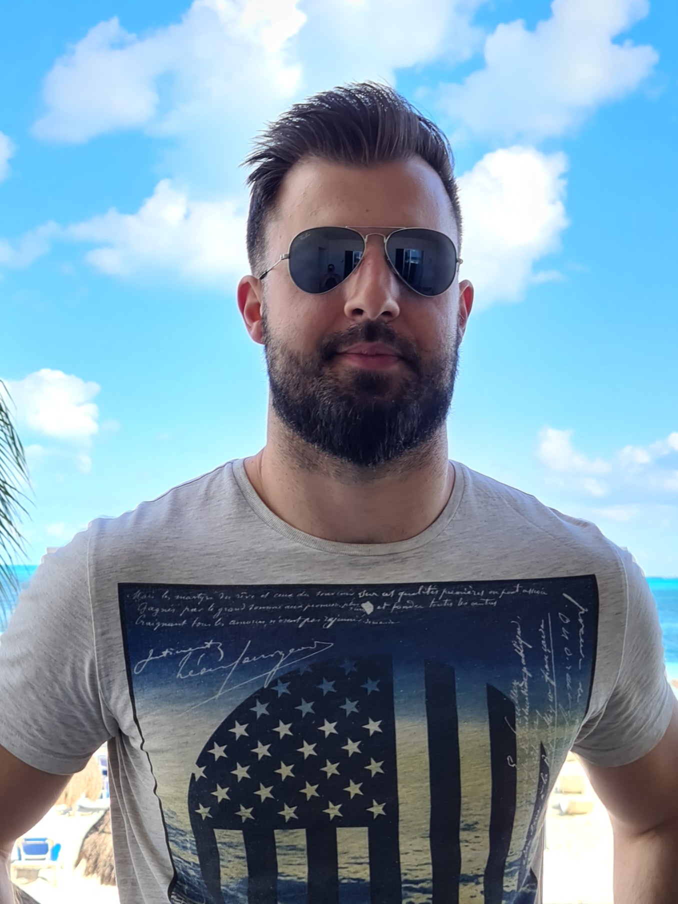 Jesse Caunter, wearing aviator sunglasses, stands in front of a bright blue sky