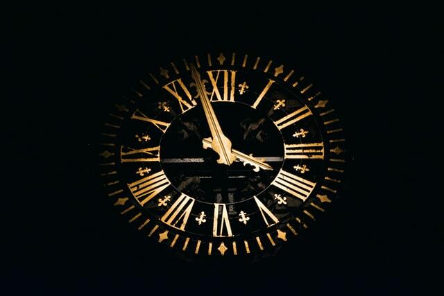 Image of a clock face with gold hands and numbers, set against a black background